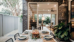 An outdoor dining area with a table set for a meal, surrounded by chairs and a large potted plant. - Gypsea at the Bay, 26b Achilles St - Wi-Fi , air con, luxury and linen (Nelson Bay)