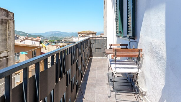 A balcony with a view of buildings and mountains, a metal railing, and a table with chairs. - Holiday Home 'Rachele' with Mountain View, Wi-Fi and Air Conditioning (Dorgali)
