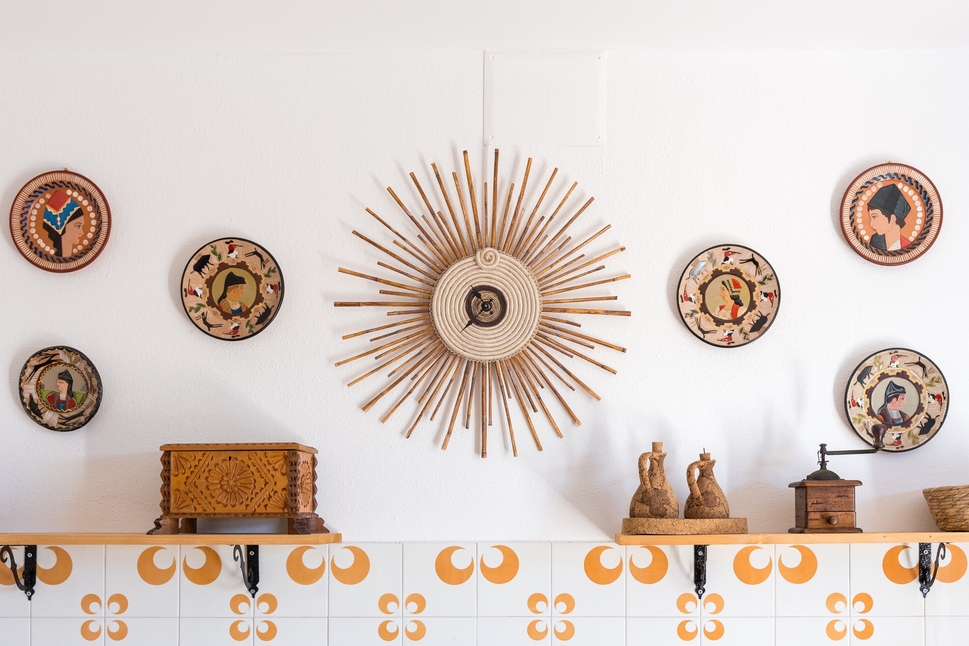 Eine Wand mit dekorativen Tellern, einer Wanddekoration im Sonnenstrahl-Design und einer Holzkiste.