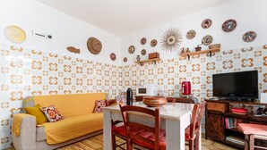 A living room with a sofa, dining table, chairs, a television, and decorative plates on the wall. - Holiday Home 'Rachele' with Mountain View, Wi-Fi and Air Conditioning (Dorgali)