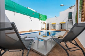 Un espace aménagé au bord de la piscine, avec deux chaises longues, une petite table avec des boissons et un patio couvert.