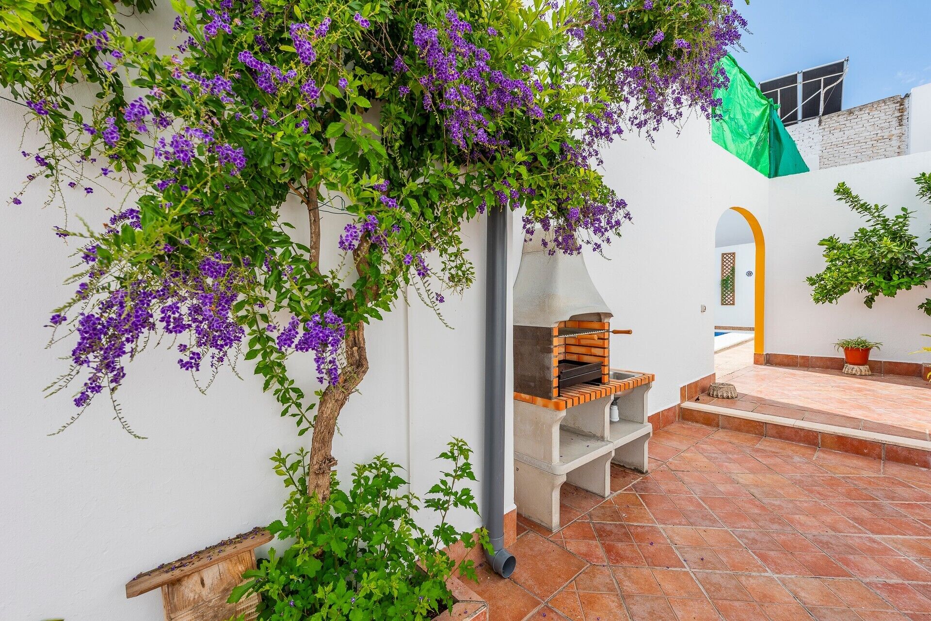 A courtyard with a brick floor, a white wall, and a wooden bench.