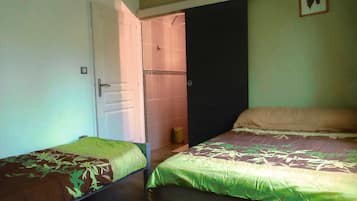 Ein Zimmer mit zwei Betten, eines mit einer grünen Tagesdecke, das andere mit einer gemusterten Tagesdecke. Eine Tür führt zu einem Badezimmer mit einer Duschvorhang.