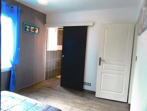 Een kamer met een bed, een deur, een badkamer met betegelde wanden, en een raam met blauwe gordijnen.