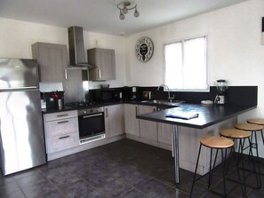 A modern kitchen with stainless steel appliances, a gas stove, a microwave, and a coffee maker. There are two stools at the island and a window providing natural light.