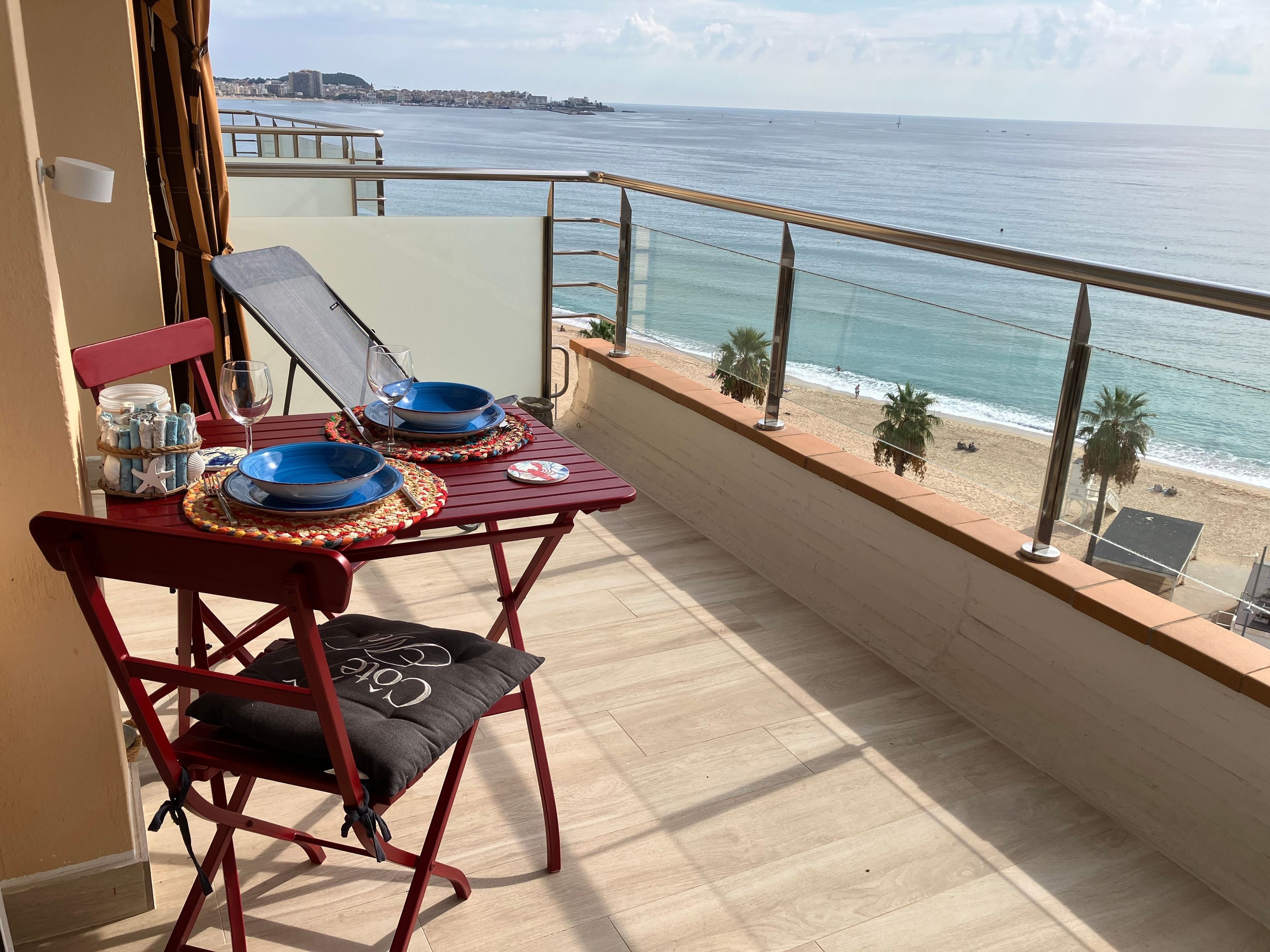 Un balcón con una mesa lista para dos personas, con vista a la playa y al mar.