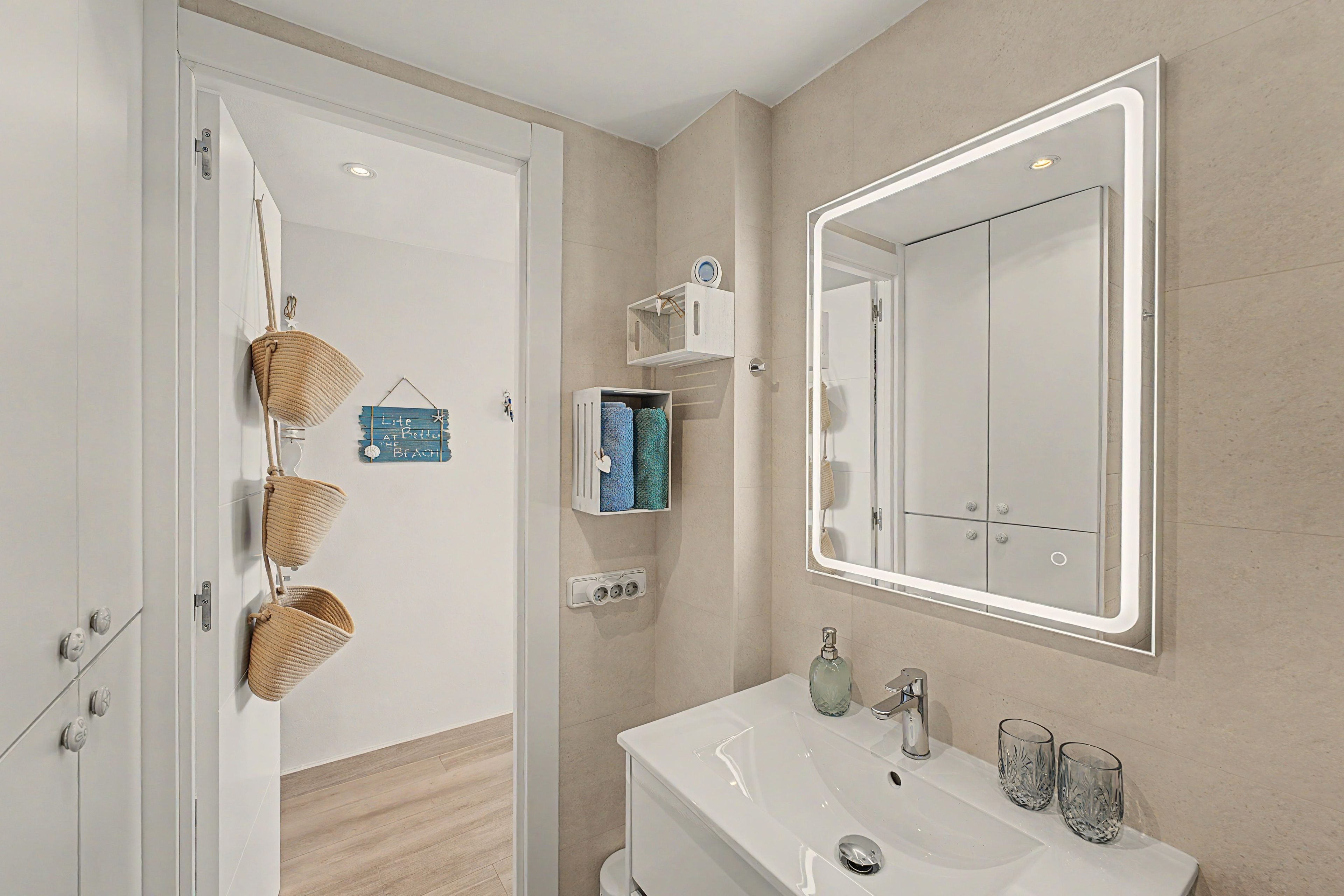 Un baño moderno con un lavamanos blanco, un espejo grande y suelo de madera.
