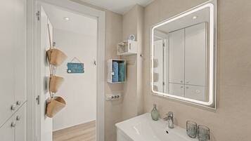 Un baño moderno con un lavamanos blanco, un espejo grande y suelo de madera.