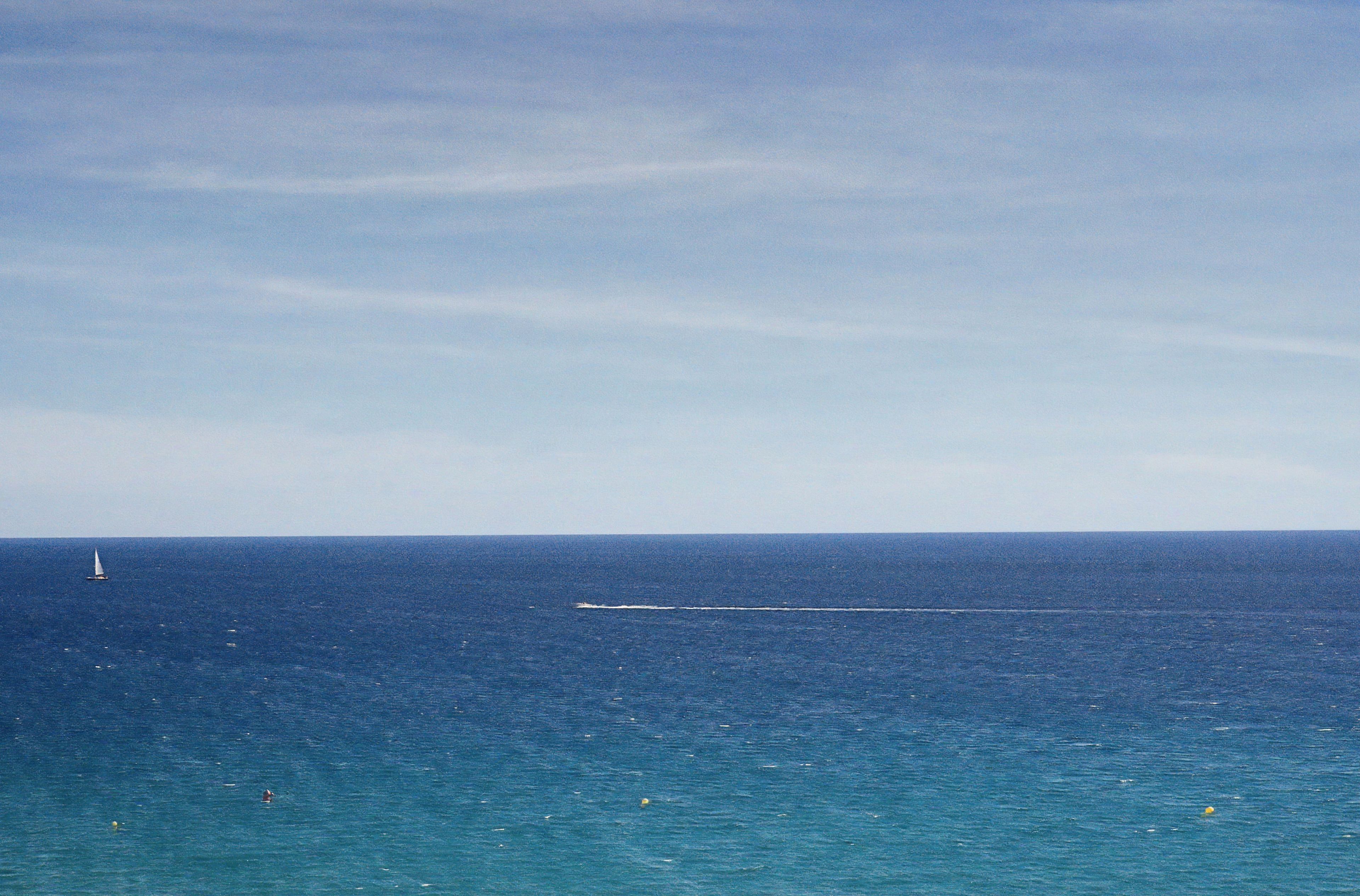 Une vue sur l’océan, avec un voilier au loin et une digue.