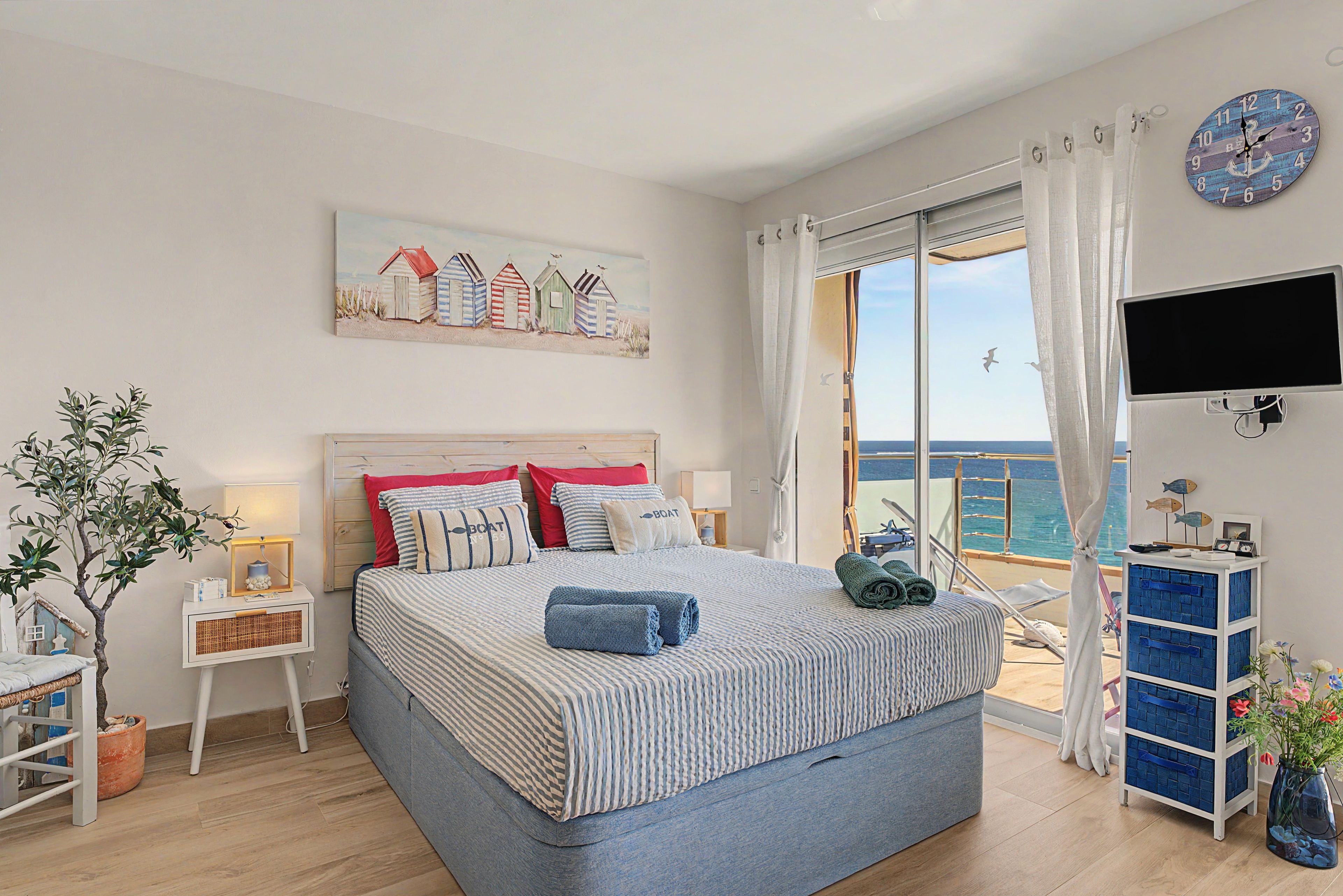 Un dormitorio con una cama, un cuadro de cabañas de playa, un televisor y vista al mar.