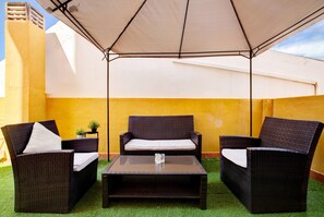 An outdoor patio with wicker furniture, a glass table, and a large umbrella.