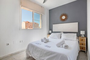 A bedroom with a large bed, a window, a wall-mounted sunburst decoration, and a bedside table with a lamp.