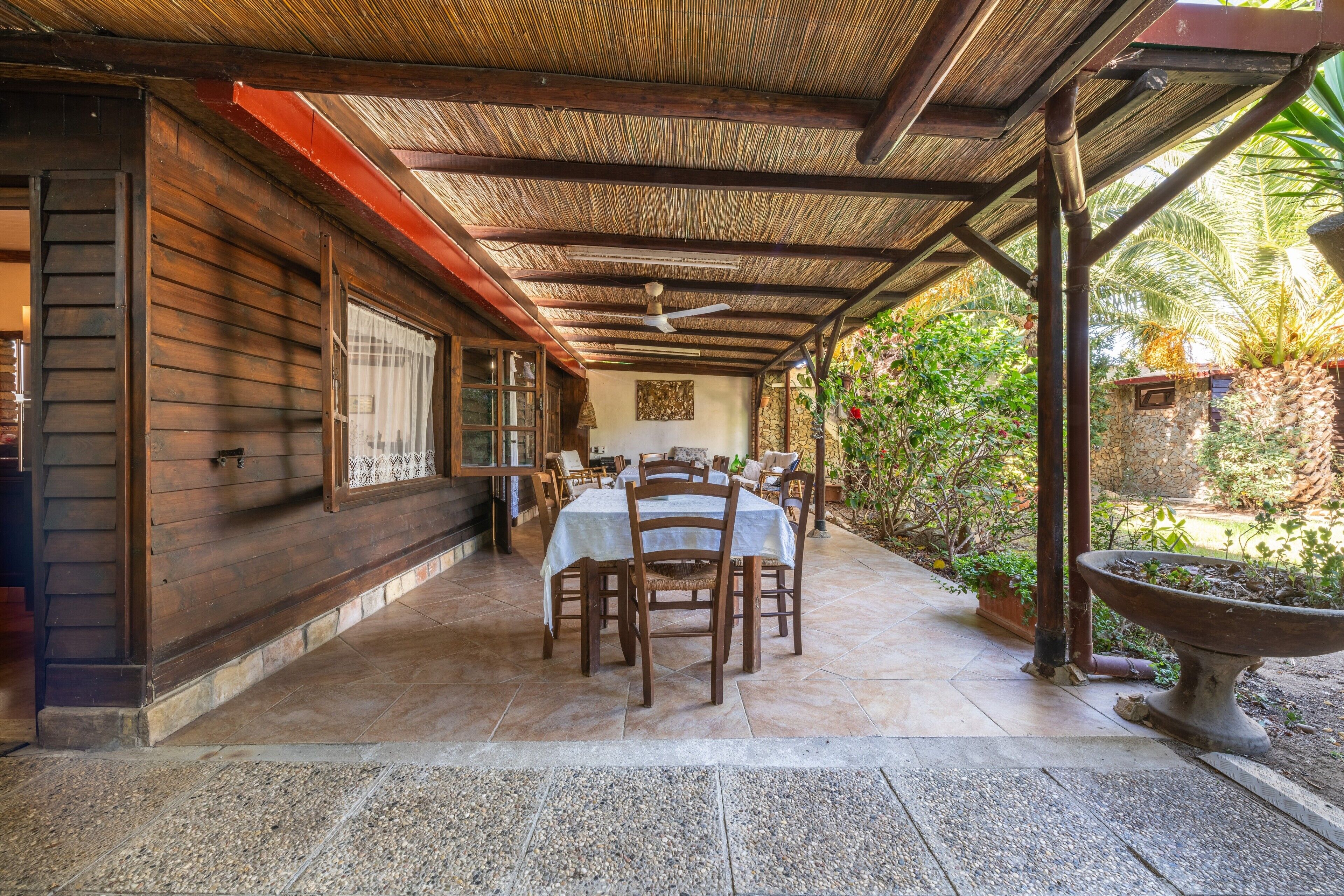 A covered patio with a table and chairs, a ceiling fan, and a stone wall.