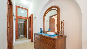Corredor que leva a um banheiro com toucador de madeira, um espelho grande e um tapete azul.