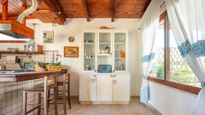 Uma cozinha com bancos de madeira, um armário com portas de vidro e uma janela com cortinas estampadas.