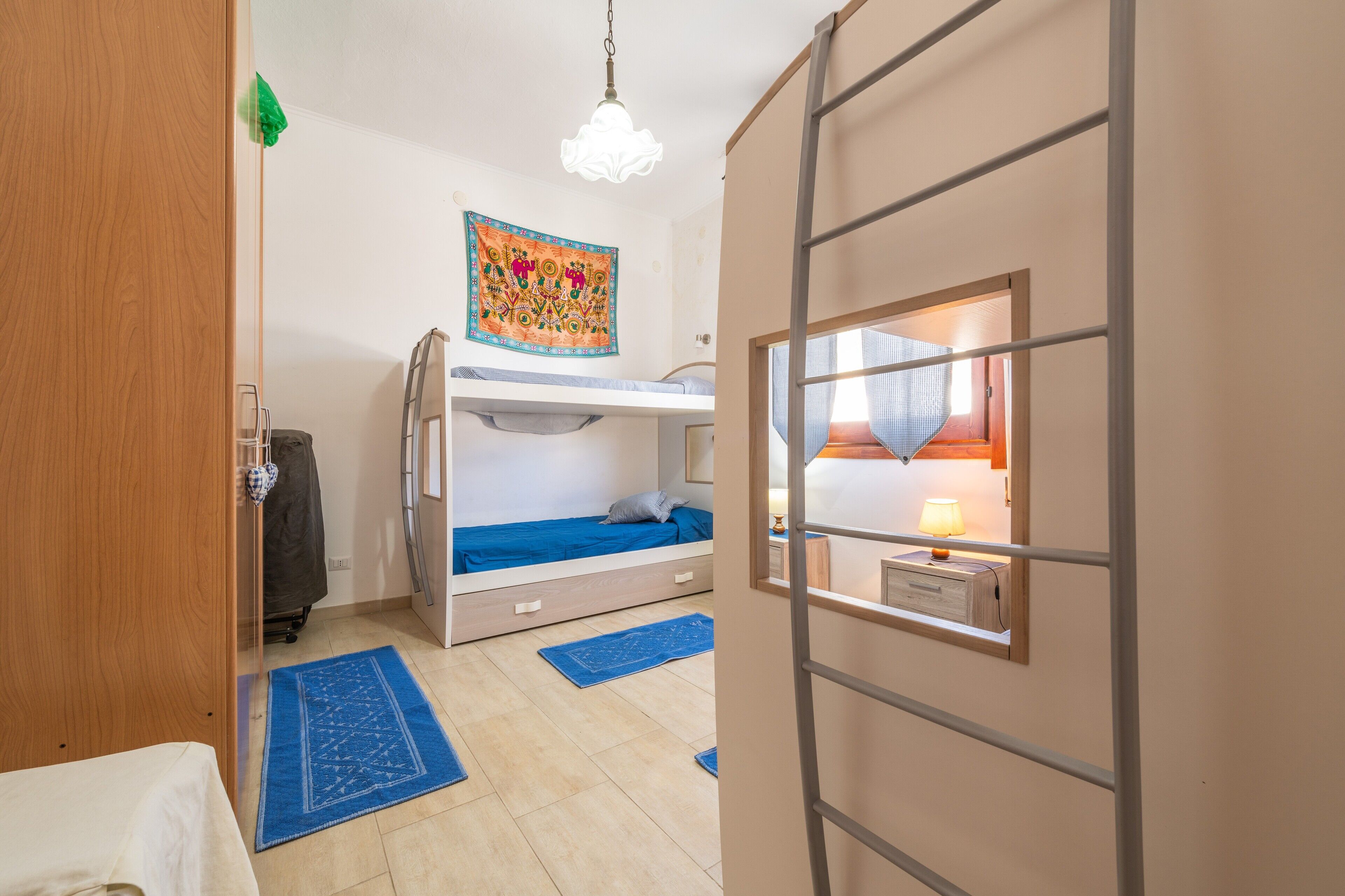 Une chambre avec un lit superposé, un bureau avec une lampe, une tapisserie au mur et une fenêtre avec des rideaux.