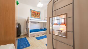 Une chambre avec un lit superposé, un bureau avec une lampe, une tapisserie au mur et une fenêtre avec des rideaux.