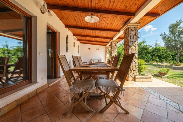 Un patio al aire libre con una mesa y sillas de madera, un pilar de piedra y vistas al jardín.
