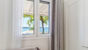 Ein Zimmer mit einem Bett, einem Fenster mit Blick auf einen Baum und ein Gewässer, sowie einer Tür.