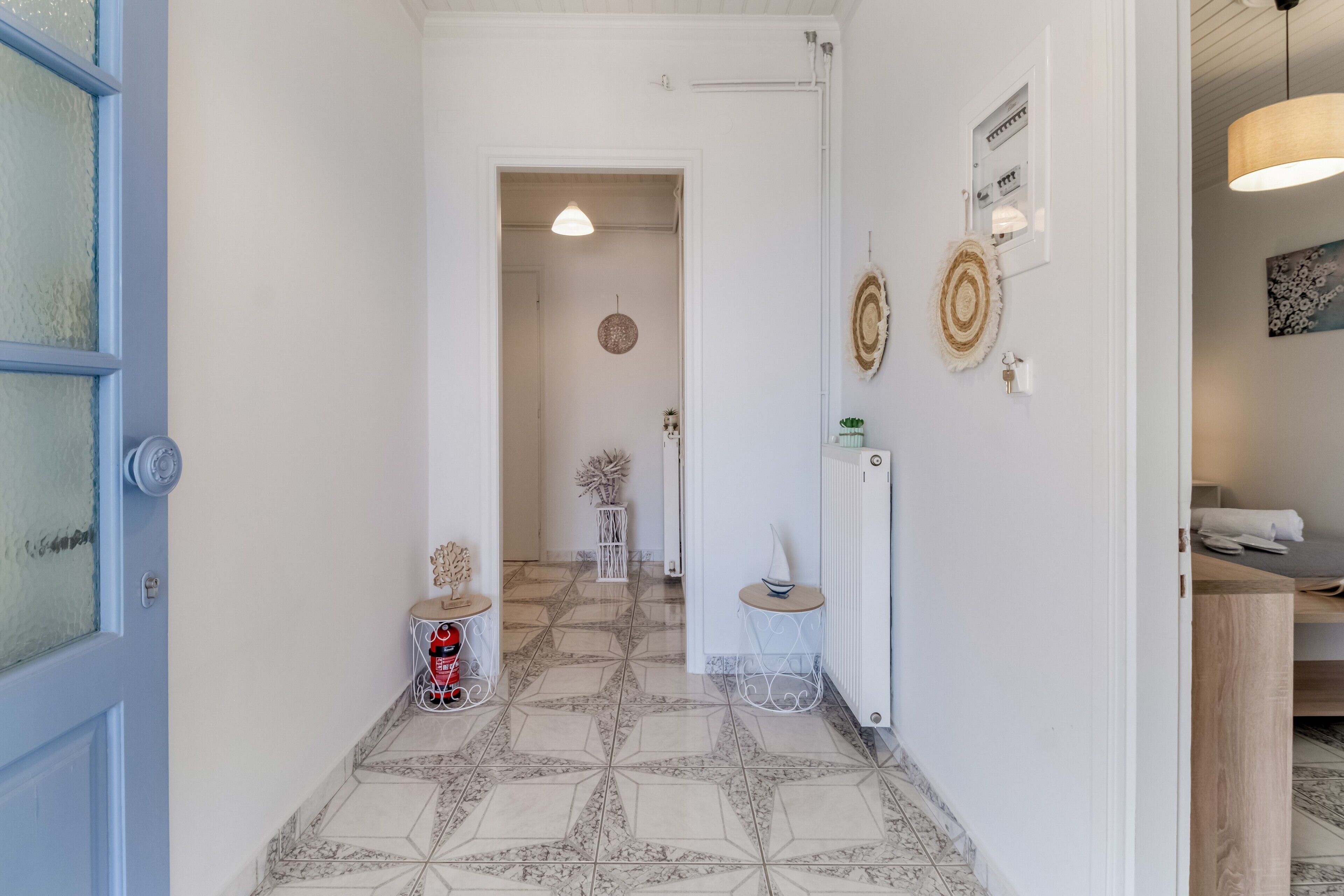 Un couloir avec des carreaux de sol à motifs, une porte bleue et un mur blanc orné d’objets décoratifs.