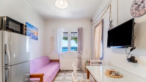 Eine kleine Küche mit einem Kühlschrank, einem Toaster, einem Esstisch mit einem Stuhl, einem Fernseher und einem Fenster mit Vorhängen.