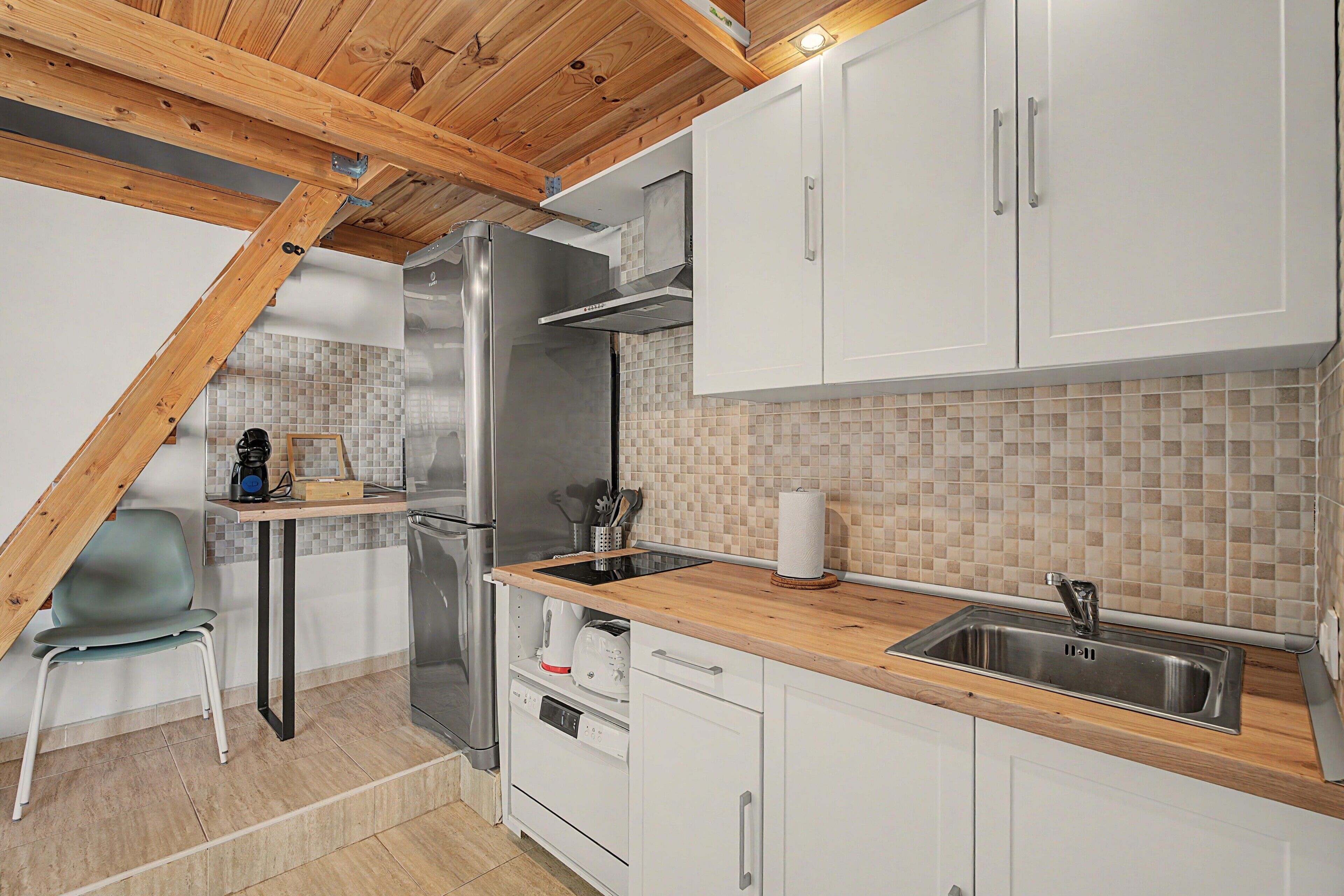 A kitchen with white cabinets, a stainless steel sink, and a wooden ceiling.