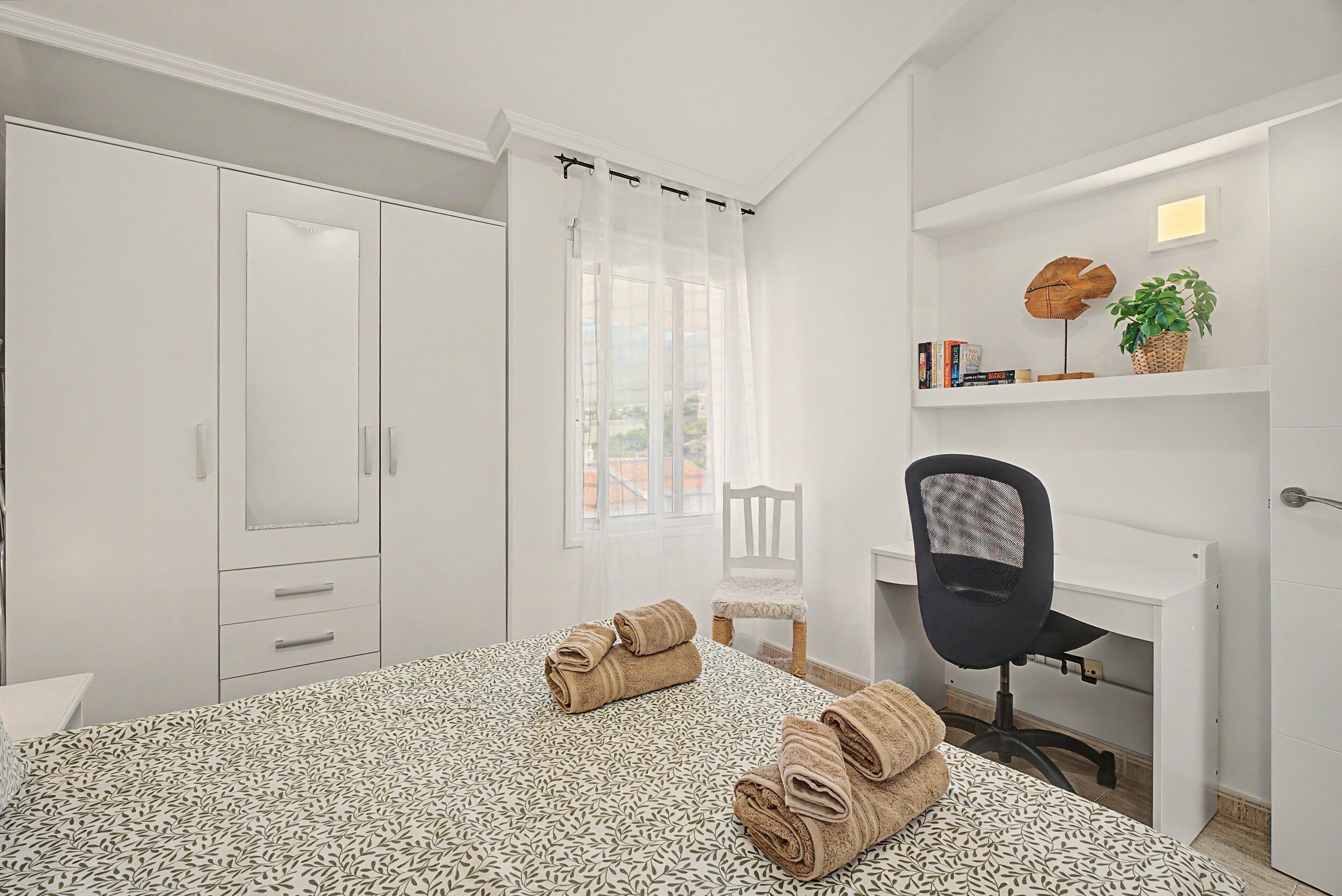Une chambre d’hôtel comprenant un lit, un bureau, une chaise, une armoire et une fenêtre avec des rideaux.