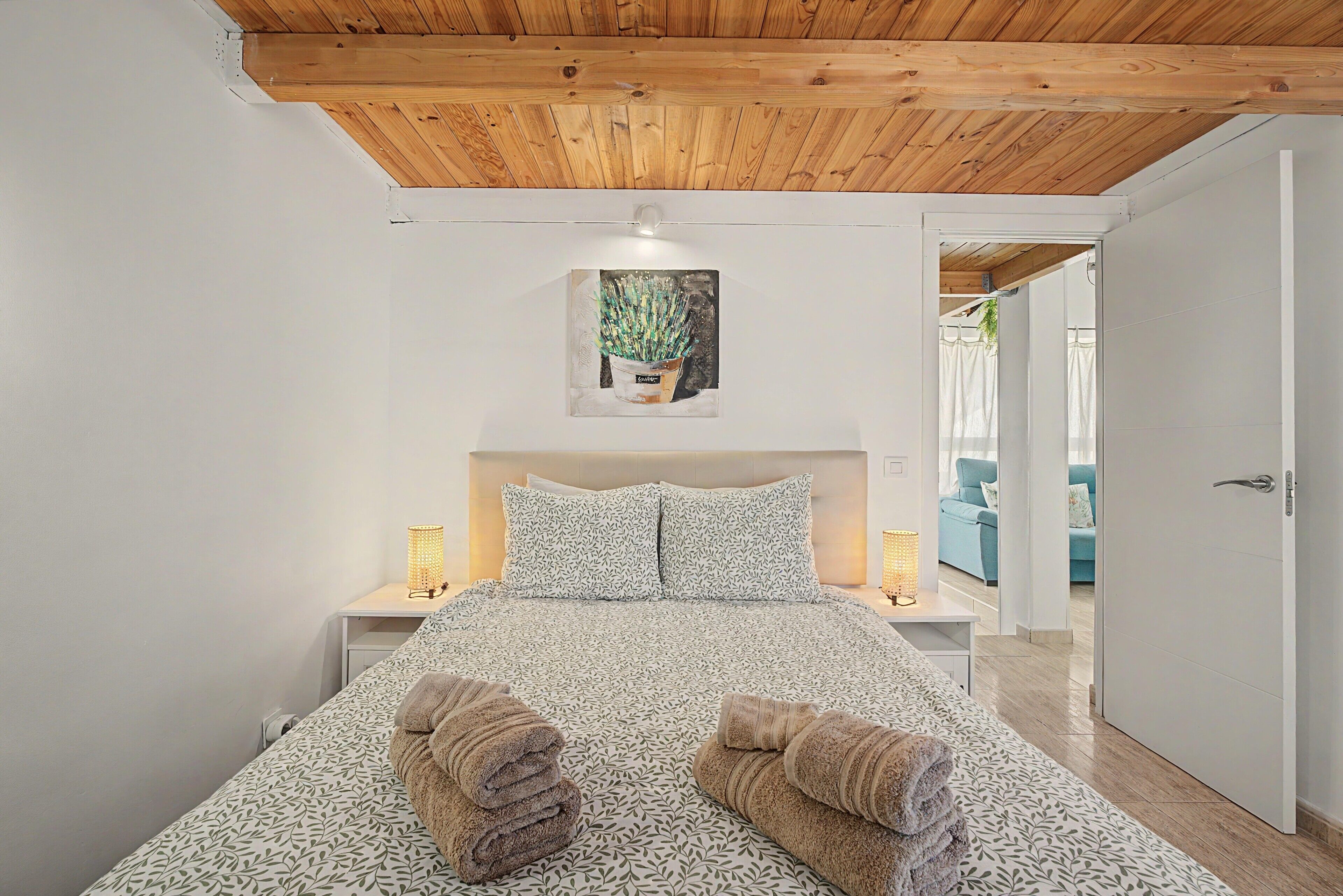 Une chambre à coucher avec un plafond en bois, un lit avec une literie à motifs, deux lampes de chevet et un tableau au mur.