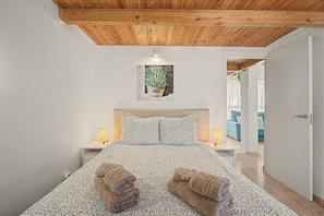 Une chambre à coucher avec un plafond en bois, un lit avec une literie à motifs, deux lampes de chevet et un tableau au mur.