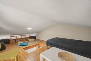 Ein Loft-Zimmer mit schrägem Dach, einer eingebauten Bank mit Kissen, einem Sofa und einem kleinen Tisch.
