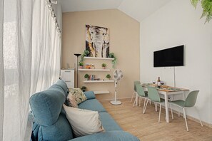 Ein modernes Wohnzimmer mit einem blauen Sofa, einem Esstisch mit Stühlen, einem Flachbildfernseher und einem Gemälde an der Wand.