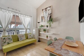 Ein modernes Wohnzimmer mit einer Couch, einem Esstisch und an der Wand befestigten Regalen mit Pflanzen.
