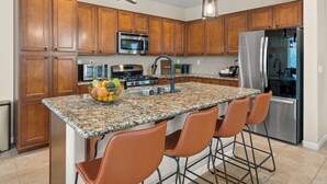 A kitchen with wooden cabinets, stainless steel appliances, granite countertops, and bar stools.