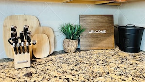 A kitchen counter with a knife block, a welcome sign, a potted plant, and a black pot.