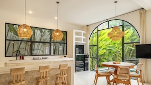 Una cocina moderna con un ventanal grande, taburetes de madera para barra y un comedor con una mesa redonda y sillas.