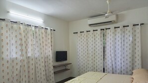 A bedroom with a bed, curtains, a TV, and an air conditioning unit.