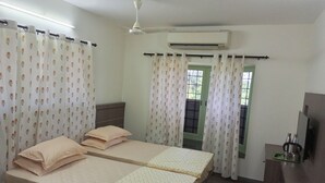 A room with two beds, a desk, an air conditioner, and a window with curtains.