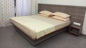 A neatly made bed with a wooden headboard, a bedside table, and a curtain with a floral pattern.