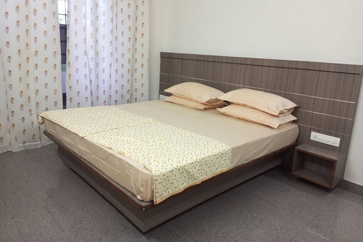 Una cama bien hecha con cabecera de madera, una mesita de noche y una cortina con estampado floral.