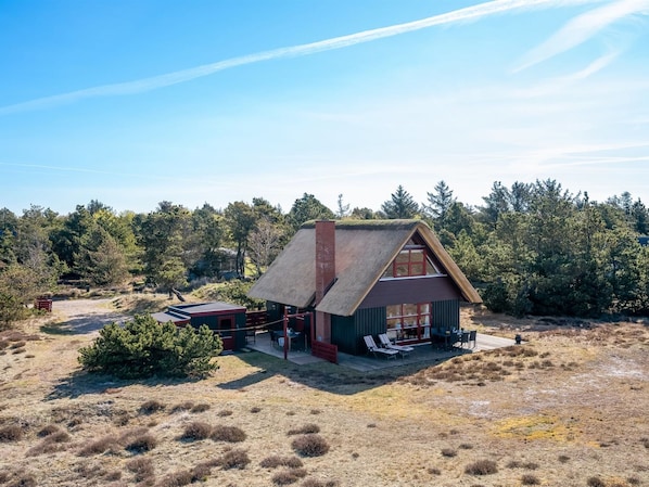 Une maison avec un toit de chaume, une terrasse et une vue sur une zone boisée.