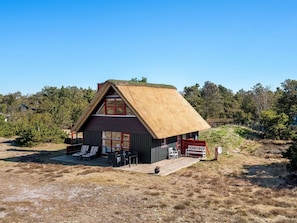 A small house with a thatched roof, a deck with lounge chairs, and a signboard.