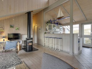 Ein modernes Interieur mit Kaminofen, Fernseher und Küchenzeile mit Barhocker.