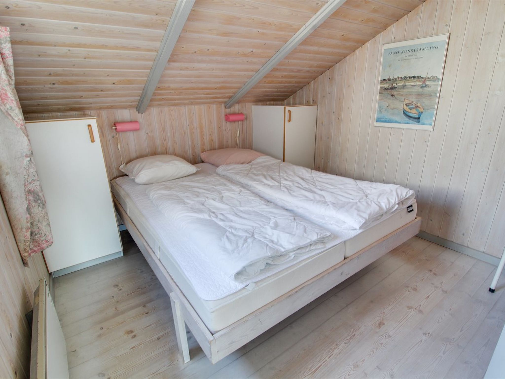 Et enkeltværelse med trævægge og -loft, en hvid seng og et billede på væggen.