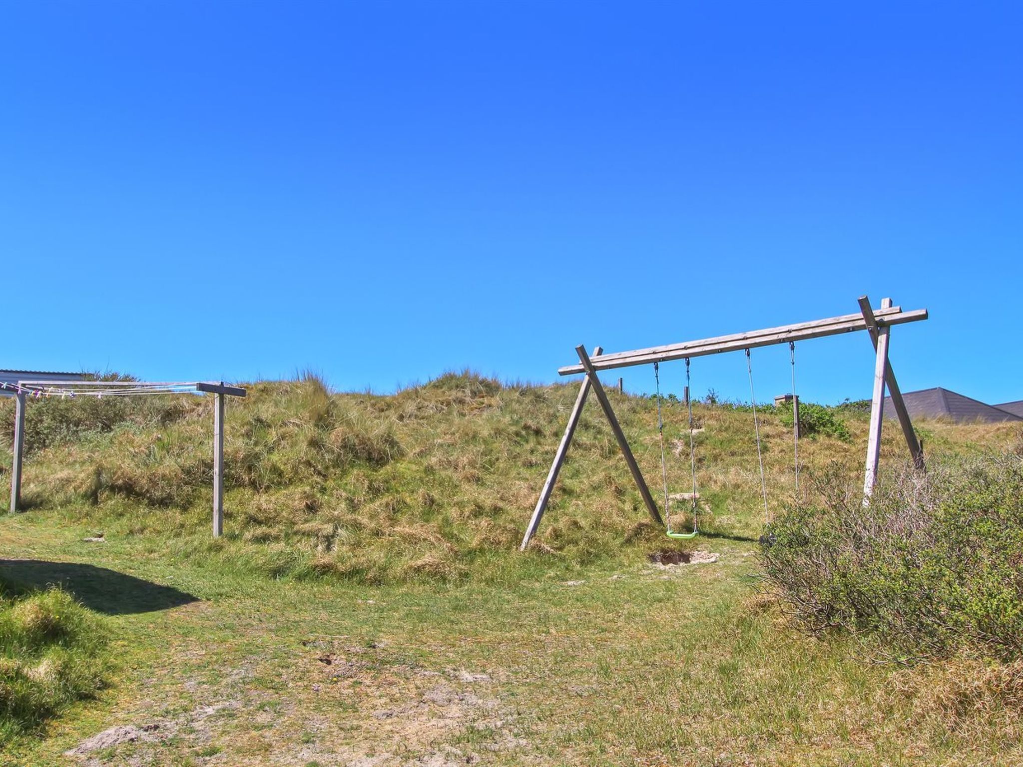 Une zone herbeuse avec des balançoires en bois et un ciel d’un bleu limpide.