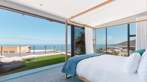 A modern bedroom with a large bed, a view of the sea, and a balcony with a lawn. - Amara 2 -designer Penthouse With Spectacular Views (Cape Town)