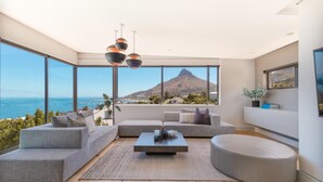A modern living room with a large window overlooking a mountain and the sea. - Amara 2 -designer Penthouse With Spectacular Views (Cape Town)