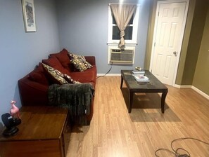 Cozy living space with a sofa, coffee table, and side table, featuring a window and air conditioning unit.