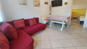Una sala de estar con un sofá rojo, una mesa a cuadros y un televisor de pantalla plana en la pared.