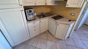 Una cocina compacta con armarios blancos, una cafetera, un lavabo y una estufa.