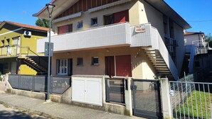 Un edificio de dos pisos con balcón, escalera y entrada protegida por una reja.